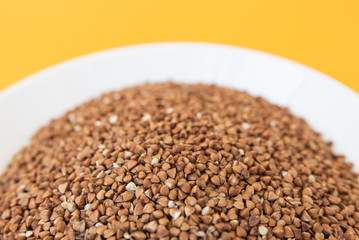 Plate with raw buckwheat on yellow background