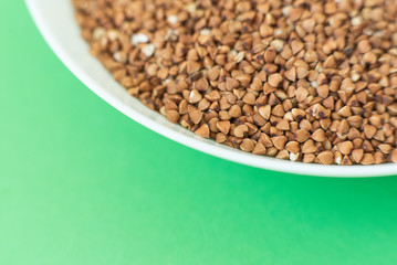 Plate with raw buckwheat on green background