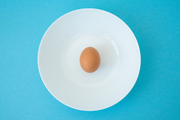 brown raw egg in white plate on blue background