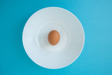 brown raw egg in white plate on blue background