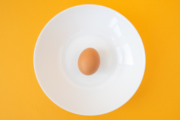 brown raw egg in white plate on yellow background