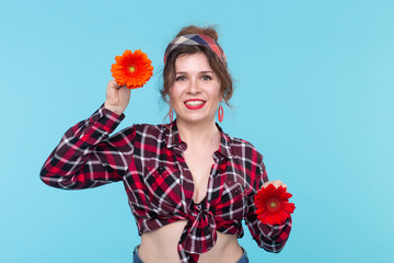 Charming young smiling woman holding two red and orange flower in her hands posing on a blue...