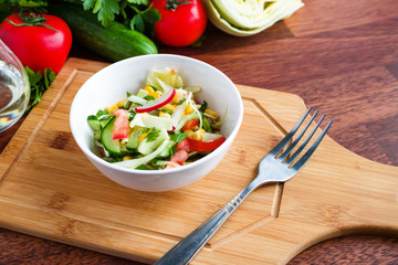 healthy fresh salad with cucumber cabbage tomato radish corn parsley in white bowl