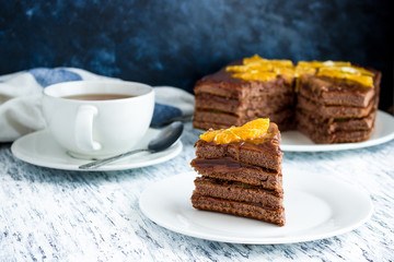 piece of  chocolate sponge cake  on white plate cup of tea on white table