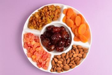 Mix of dried fruits and nuts on a white plate. Apricot, almond, raisin, dates fruit. On a lilac background. Space for text or design.