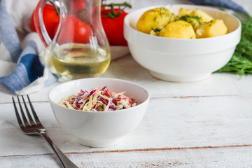 fresh coleslaw salad boiled potato with dill  glass bottle of oil fork on wooden table