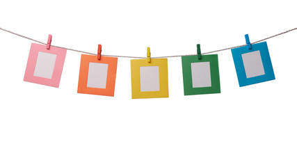 Five multicolored paper photo frames hanging on the rope with wooden clothespins isolated on white...