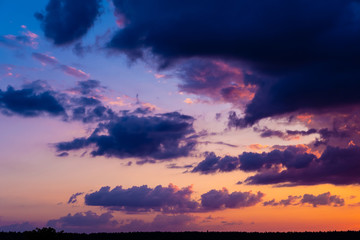 Fototapeta na wymiar Evening sky at sunset background. Dark clouds hanging above horizon. Majestic cloudscape in blue, orange, violet shades. Grey cloudlets bringing rain. Countryside skyline in twilight time