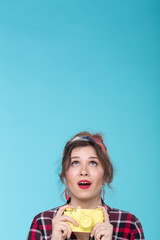 Positive beautiful young woman in retro style holding a yellow film camera in her hands and looking up. Concept space for advertising and information from above.