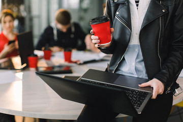 Cropped Portrait Of Successful Business Woman in casual wear Holding red Cup Of Hot Drink In Hand and working on laptop. Young coworkers working together