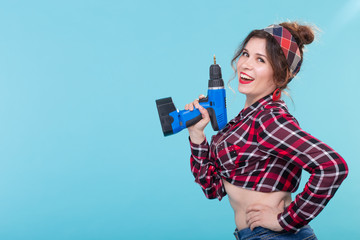 Cool positive young woman in a plaid shirt holding a screwdriver posing on a blue background with copy space. Concept of repair and construction.