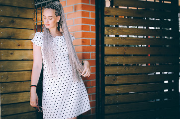 Girl on vacation with braided pigtails gray light shade of Zizi on a Brick and wooden background in a light dress