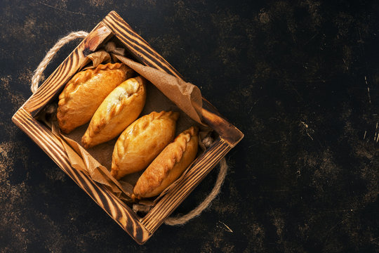 Traditional Russian pies in a wooden tray on a dark rustic background. Russian pirozhki ,baked patties. Top view, copy space, flat lay.
