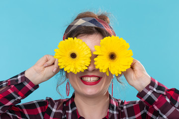 Close-up positive smiling young woman in a red checkered shirt holding yellow flowers on her eyes...