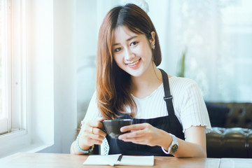 Obraz premium Portrait of young beautiful woman holding cup of coffee with notebook on wooden table in cafe