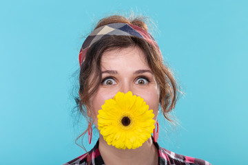 Funny positive young woman in retro image holding a bright yellow gerbera flower in her teeth...