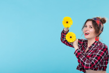 Charming smiling young positive woman in a plaid shirt holding bright yellow flowers in her hands posing on a blue background with copy space. Concept information and link to the right.