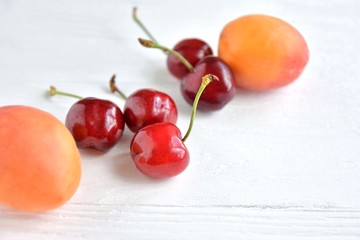 Juicy red cherries and fresh tasty apricot with selective focus on textured neutral background. Seasonal fruits and berries. Harvest of apricot and sweet cherries on white table. Picking summer fruits