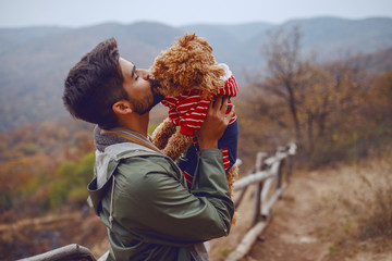 Attractive mixed race man kissing his loving dog while standing in nature at fall.