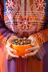 the woman wearing traditional clothes holds hazelnuts in the bowl.