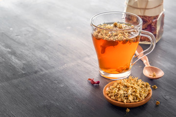 Herbal tea with pharmaceutical chamomile and rose petals on a gray wooden table. Copy space