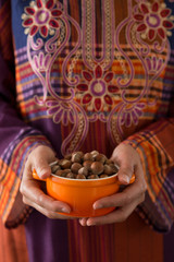 the woman wearing traditional clothes holds hazelnuts in the bowl.