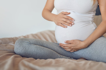 Young pregnant woman cradling her baby bump or belly with her hands in a close up cropped view conceptual of maternal love