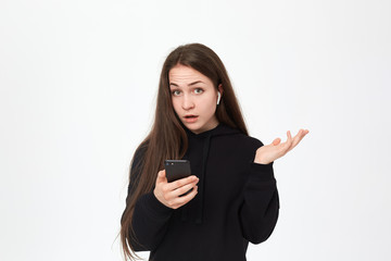 Fototapeta premium Studio shot of a beautiful young brunette woman with wireless headset holding mobile phone and looking at the camera while standing over white background.