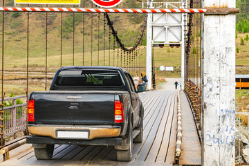 Pickup truck passing over a suspension bridge over a mountain river