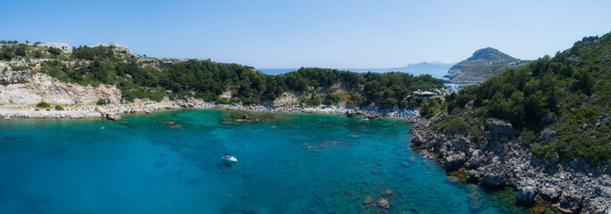 Obraz premium Sunny beach lagoon with rocky coastline, Greece. Tourists under umbrella chill relax near clear blue emerald turquoise sea water