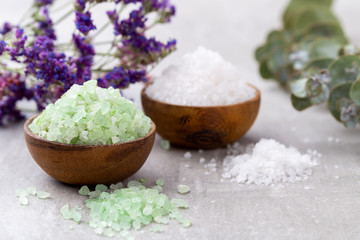 Sea salt in bowl, aroma oil in bottles, Wellness and flowers on grey textured background and flowers on vintage wooden background. Selective focus.