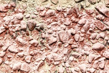 Stone rubble in a concrete wall painted with red paint as a background