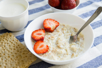 Oatmeal porridge with fresh strawberries in white bowl. Healthy breakfast, fruits and milk for breakfast wit kefir. 