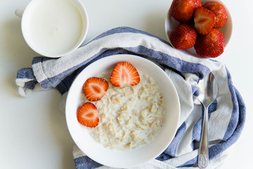 Oatmeal porridge with fresh strawberries in white bowl. Healthy breakfast, fruits and milk for breakfast wit kefir. 
