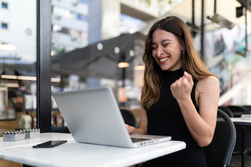 Business woman work process concept. Young woman working university project with generic design laptop. Happy excited woman at home workstation. Blurred background, film effect.