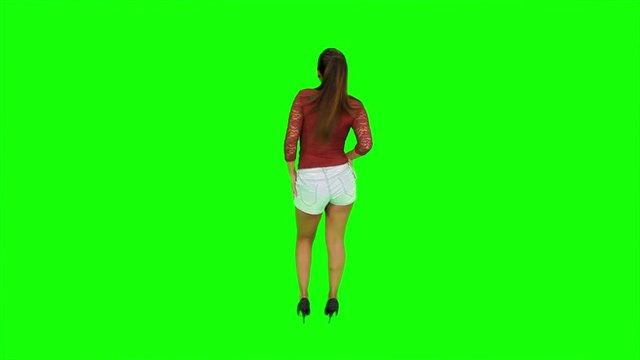Sexy woman Model with sexy ass dancing back and shaking ass in front of a green screen with black high heels, blue jean shorts and red top. Static large shot. 4K.