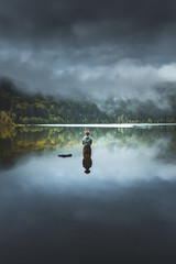 Amazing rear view reflection of a man standing on rock in the middle of a lake. Folk scenery concept with cloudy sky and and stunning fog conditions right above Sfanta Ana lake, Transylvania, Romania