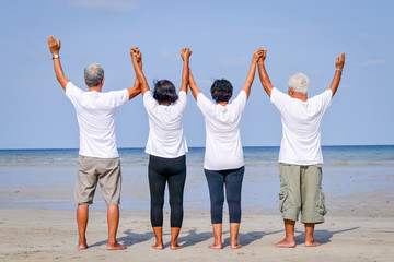 Obraz premium Happy group of elderly friends come to rest at the sea Standing, holding hands and facing the sea