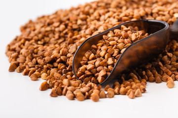 Food ingredients: heap of buckwheat in a wooden scoop, on white background