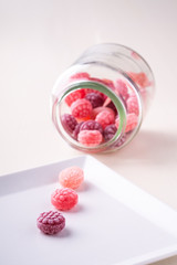 Three candy canes on white plate with candy canes sweets in form of juicy berries in glass jar on white background isolated