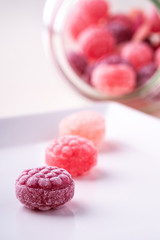 Three candy canes on white plate with candy canes sweets in form of juicy berries in glass jar on white background isolated