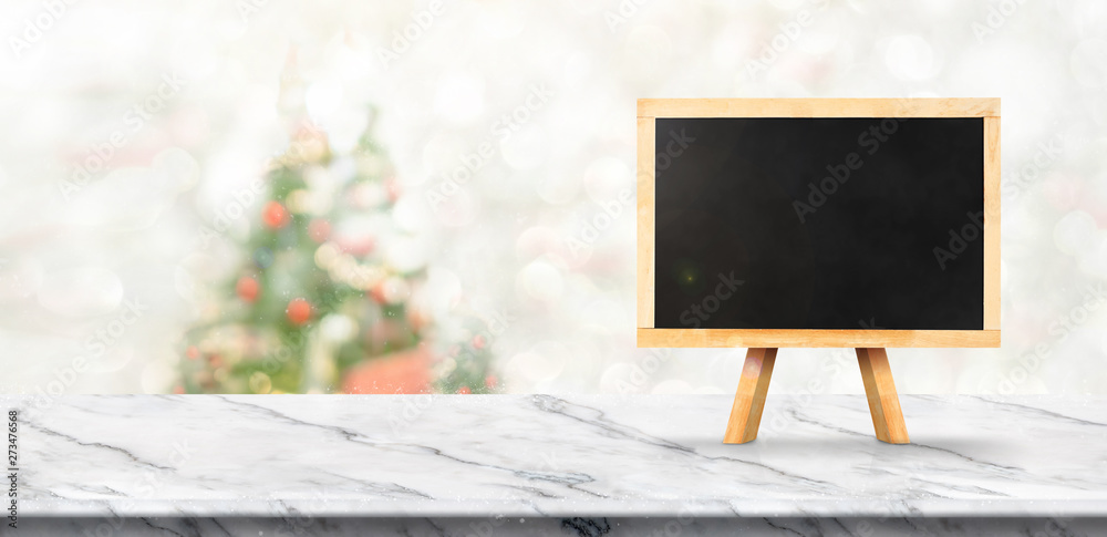 Poster merry christmas banner,Mock up blackboard on white marble table with blur christmas tree and snow fall background with bokeh light. banner for display of product.