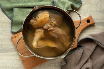 Chicken bouillon. Chicken meat is cooked in a broth pan. Chicken broth in the kitchen on a wooden background. Dietary dish in the pan.