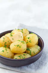 New young boiled  potato topped with melted butter and chopped dill, in ceramic bowl, vertical, copy space