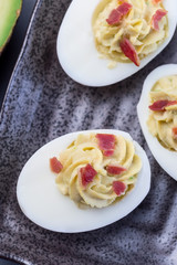Deviled eggs stuffed with avocado, egg yolk and mayonnaise filling, garnished with bacon, vertical, top view
