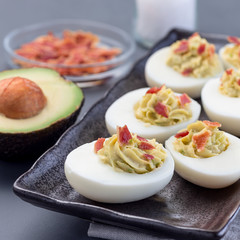 Deviled eggs stuffed with avocado, egg yolk and mayonnaise filling, garnished with bacon, square