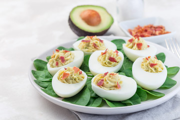 Deviled eggs stuffed with avocado, egg yolk and mayonnaise filling garnished with bacon on spinach leaves, horizontal, copy space