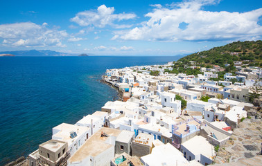 Fototapeta na wymiar panoramic view from the hill at the Mandrakion city, traditional Greece city whith white houses and blue doors and window shutters between blue sea and green mountains and blue sky in Nisyros Island