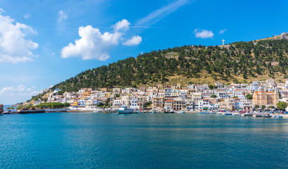 Fototapeta na wymiar view at the sea at the shore and colored houses on the beach against the green hills with trees on the island of Kalymnos in Greece
