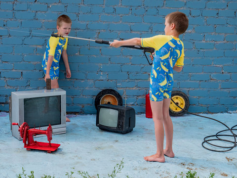 Funny children in swimsuits for boys posing in front of camera on background of brick wall with high-pressure washer. Children hold hammers and sledgehammers and try to break the TV
